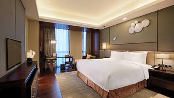 A hotel room with a large bed, a desk, a television, and a wall-mounted lamp.