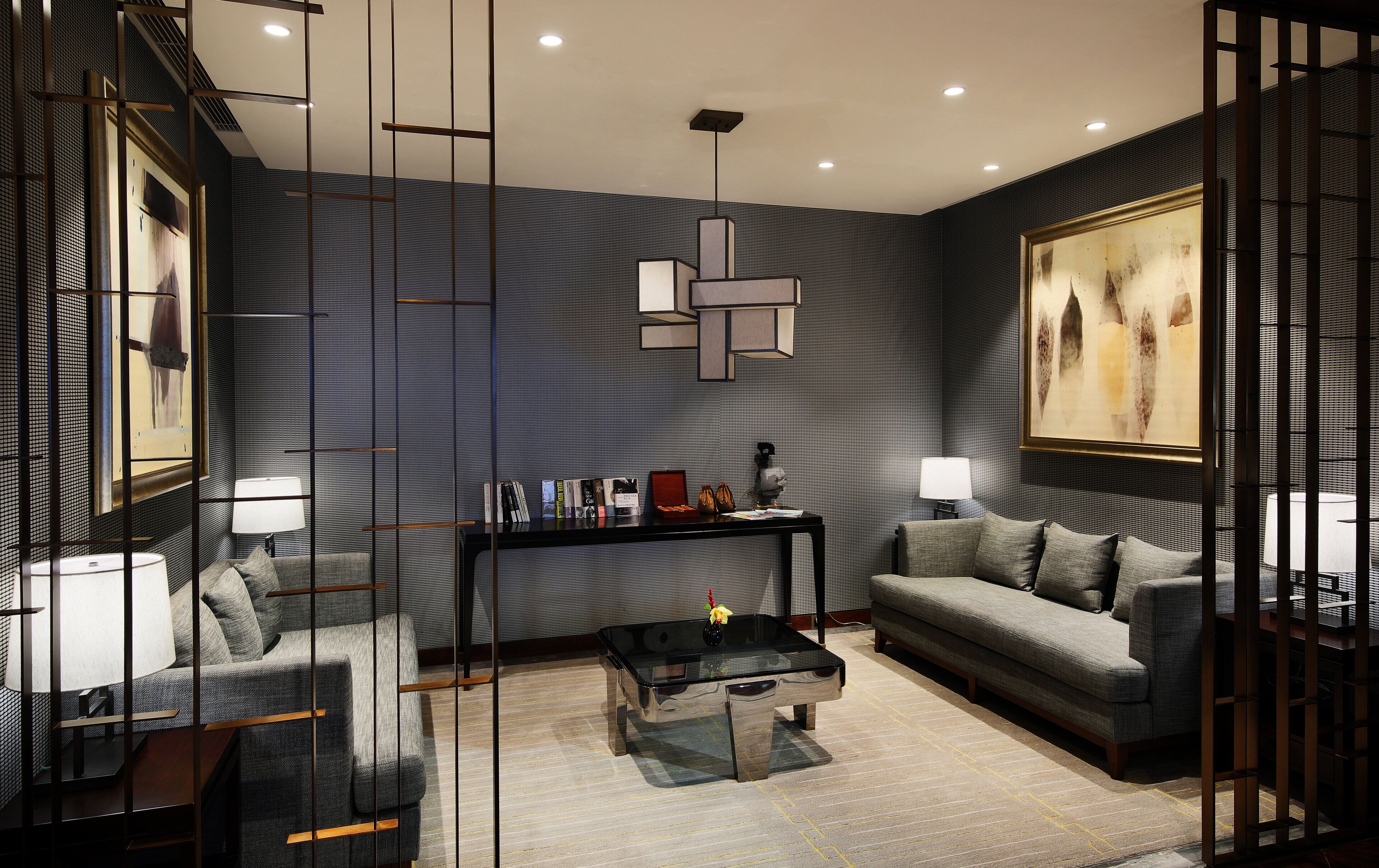 A modern living room with a sofa, armchair, and coffee table, featuring a geometric light fixture and artwork on the walls.
