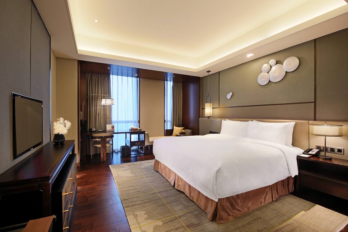 Ein Hotelzimmer mit einem großen Bett, einem Schreibtisch, einem Fernseher und einer Wandlampe.