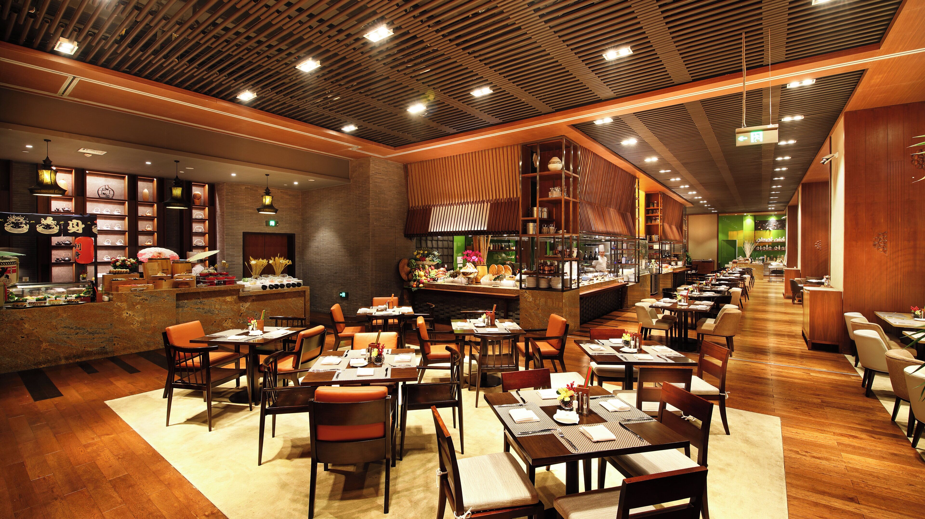 A restaurant interior with wooden flooring, multiple dining tables and chairs, a bar area, and a kitchen visible through a glass partition.