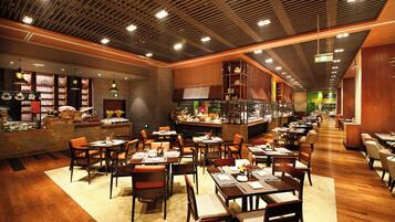 A restaurant interior with wooden flooring, multiple dining tables and chairs, a bar area, and a kitchen visible through a glass partition.