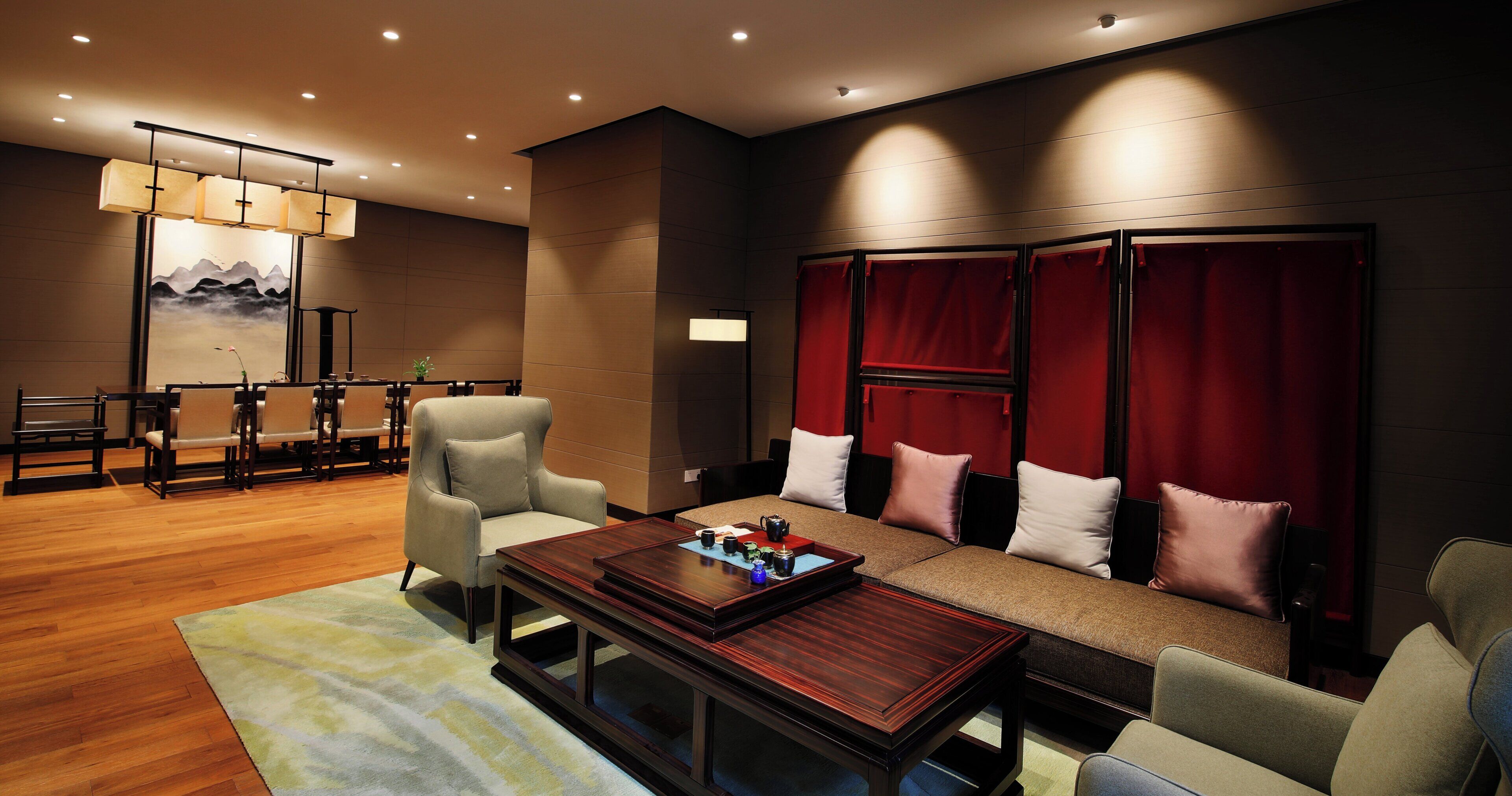 A modern hotel room with a wooden floor, a sofa with cushions, a coffee table, and a dining area with chairs and a table.