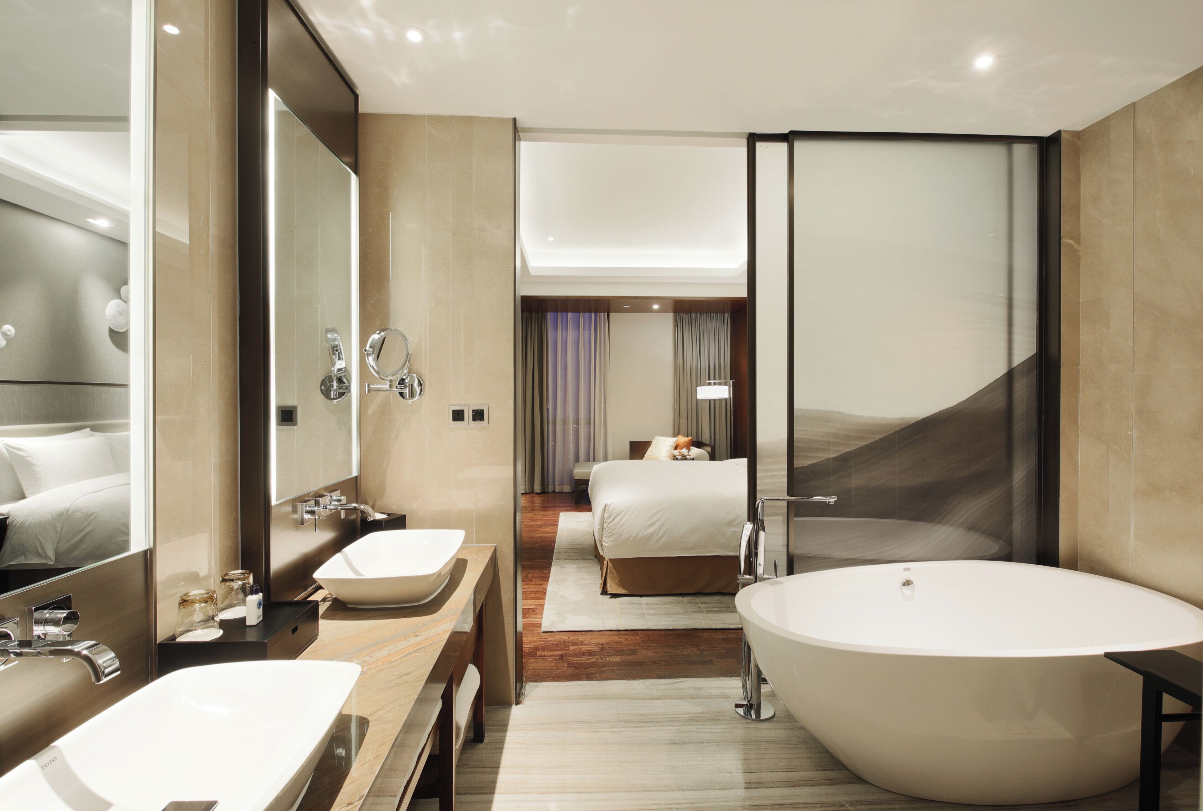 A modern hotel bathroom with a large bathtub, two sinks, and a mirror.
