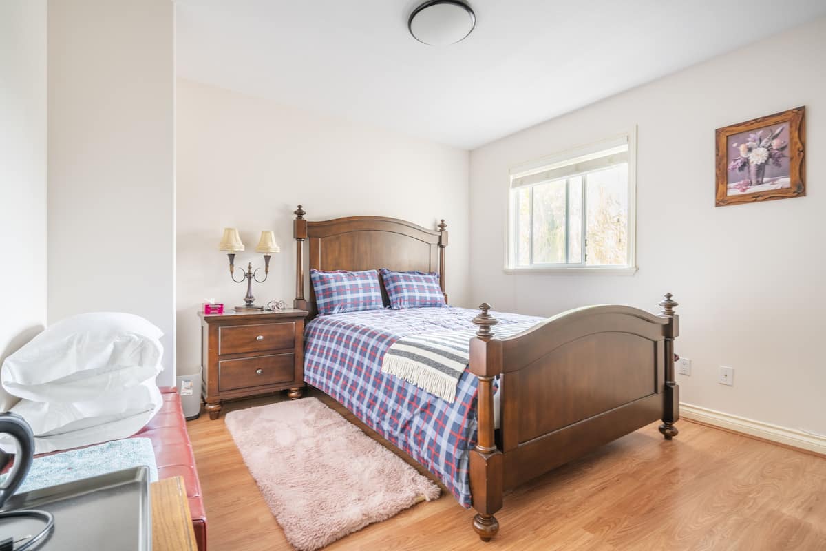 Un dormitorio con una cama de madera, una mesita de noche con lámparas, un aparador y una ventana con luz natural.