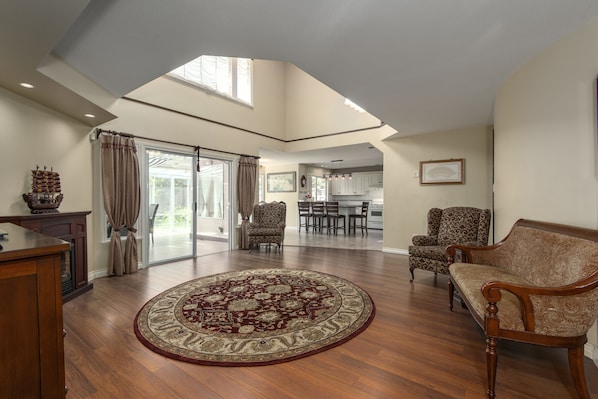 A spacious living room with a large wooden floor, a round patterned rug, and a high ceiling with skylight.