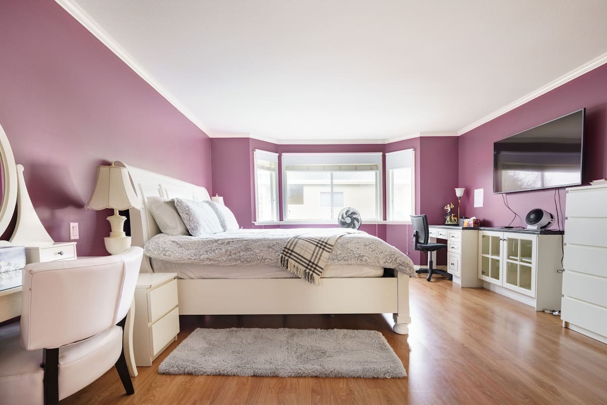 Un dormitorio con cama, mesita de noche, lámpara, silla, escritorio y televisor.
