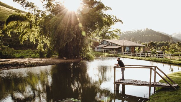 A serene lakeside setting with a wooden dock, a small boat, and a building with a sloped roof in the background. - Pousada Monteiro (Valenca)