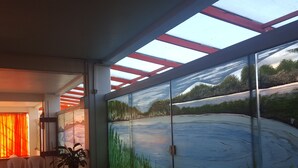 Habitación con un amplio ventanal que muestra un cuadro de un paisaje con un lago y árboles.