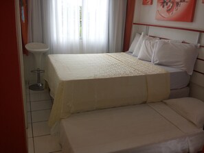 Una habitación de hotel con una cama, una mesita redonda y un ventanal con cortinas.