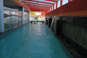 Una piscina interior con agua cristalina, una pared de vidrio en un lateral y una estructura de techo rojo y blanco.