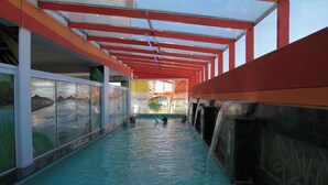 Una piscina interior con agua cristalina, vigas estructurales rojas y blancas y paredes de vidrio con obras de arte.