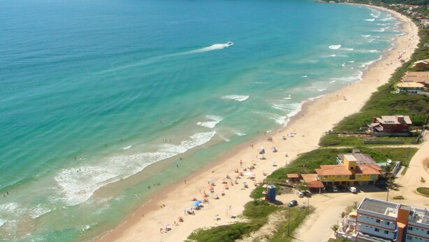 Una playa costera con aguas transparentes, una orilla arenosa y edificios a lo largo de la costa.