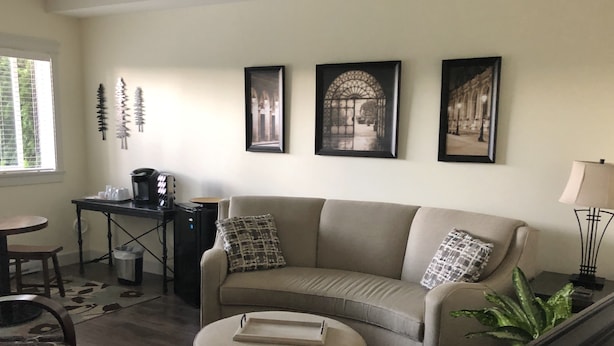 A living room with a sofa, ottoman, coffee table, and a desk with a computer. There are three framed pictures on the wall.