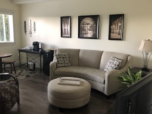 A living room with a sofa, ottoman, coffee table, and a desk with a computer. There are three framed pictures on the wall. - Private Suite in Cowichan Country (Duncan)