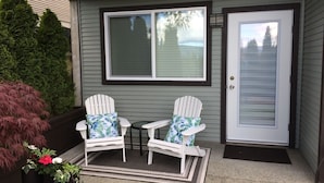 A porch with two Adirondack chairs, a small table, and a door.