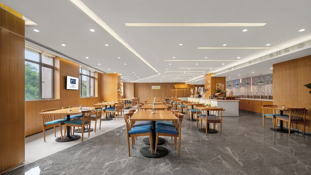 En rummelig restaurant med flere spiseborde, stole, en midterplaceret disk og store vinduer.