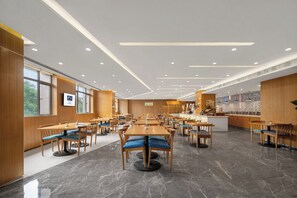 Un restaurant spacieux, doté de nombreuses tables et chaises, d’un comptoir central et de grandes fenêtres.