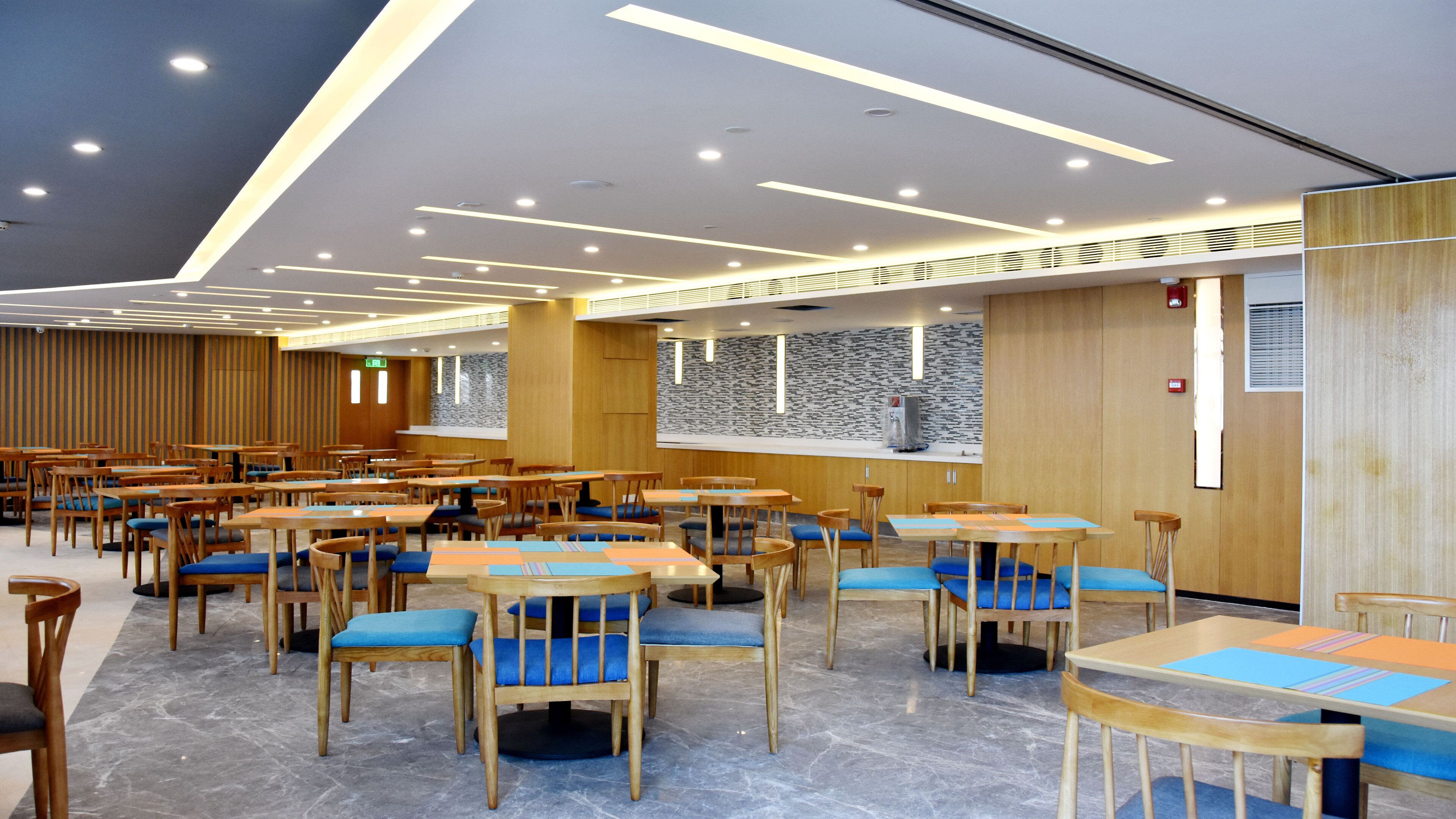 A spacious dining area with multiple tables and chairs, a high ceiling with recessed lighting, and a wooden accent wall.