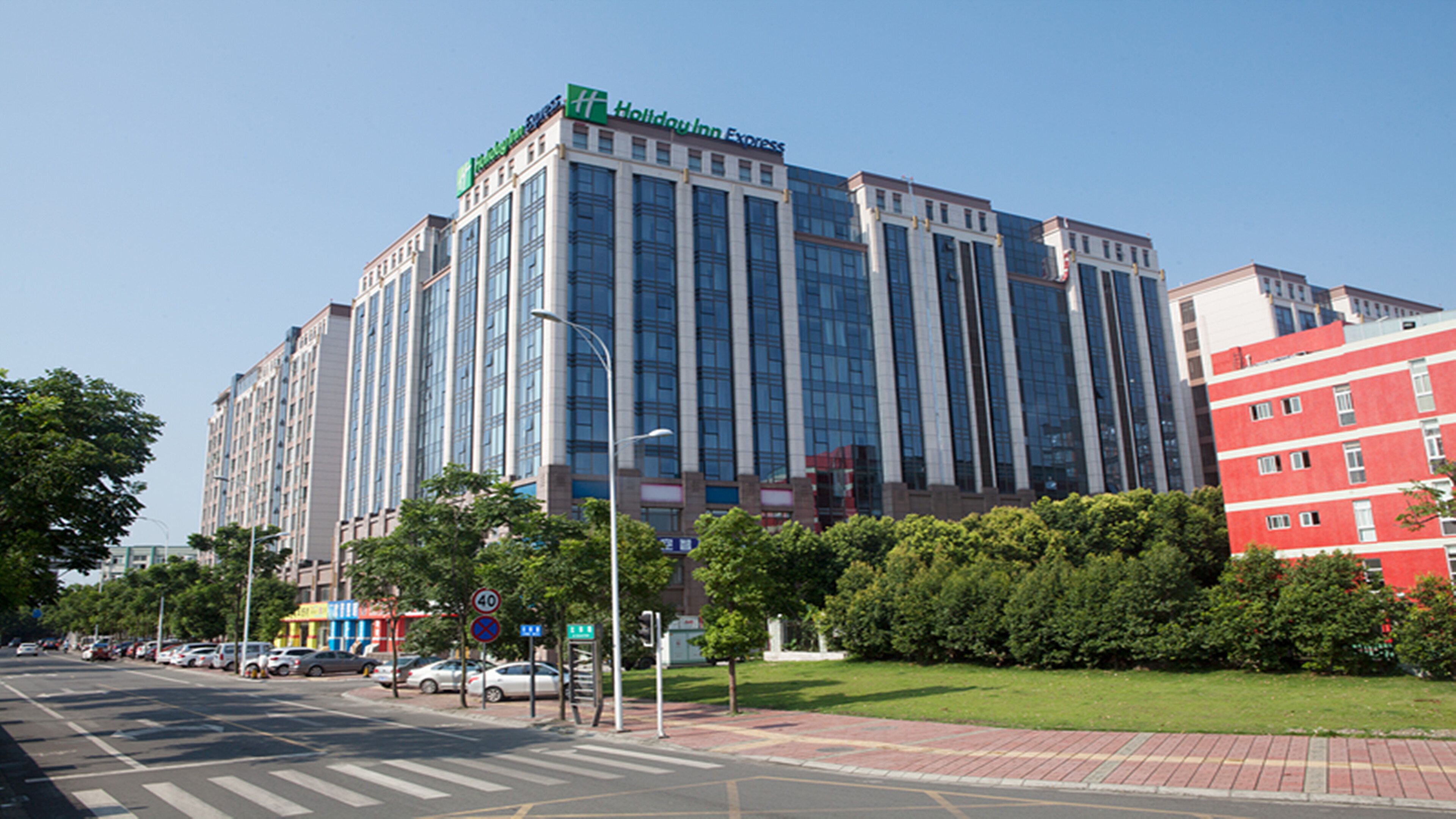 A multi-story building with a prominent 'Holiday Inn Express' sign, surrounded by greenery and a clear sky.