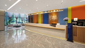 Et moderne hotelreception område med en buet skranke, et siddeområde med en sofa, og et stort vindue med udsigt over grønne områder.