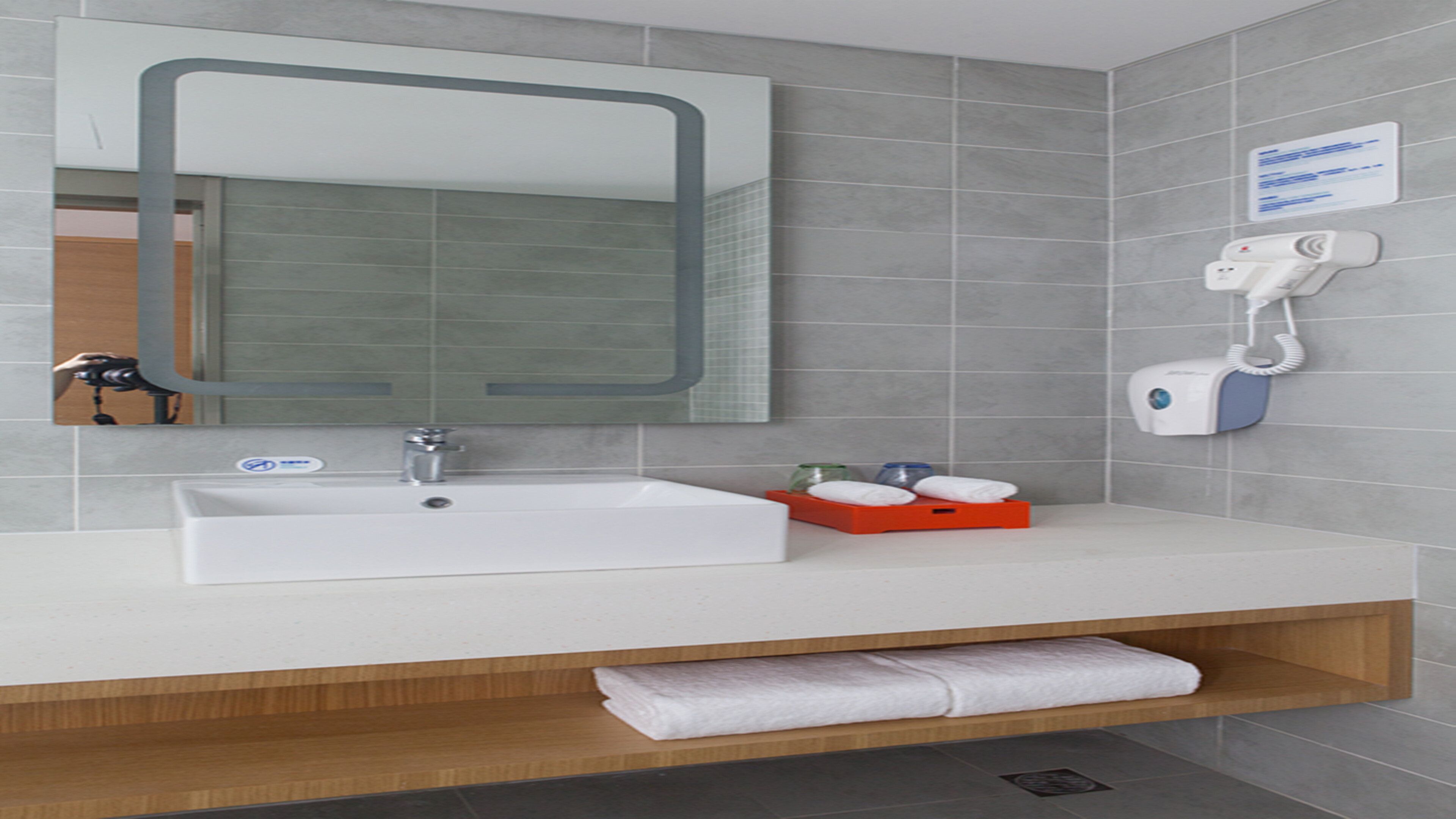 Ein modernes Badezimmer mit einem weißen Waschbecken, einem Spiegel und einem Handtuchhalter.