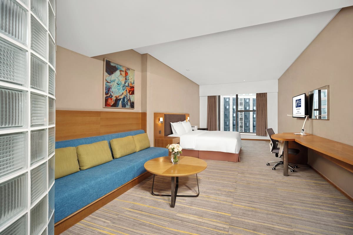 A hotel room with a bed, a sofa, a desk, and a large window.