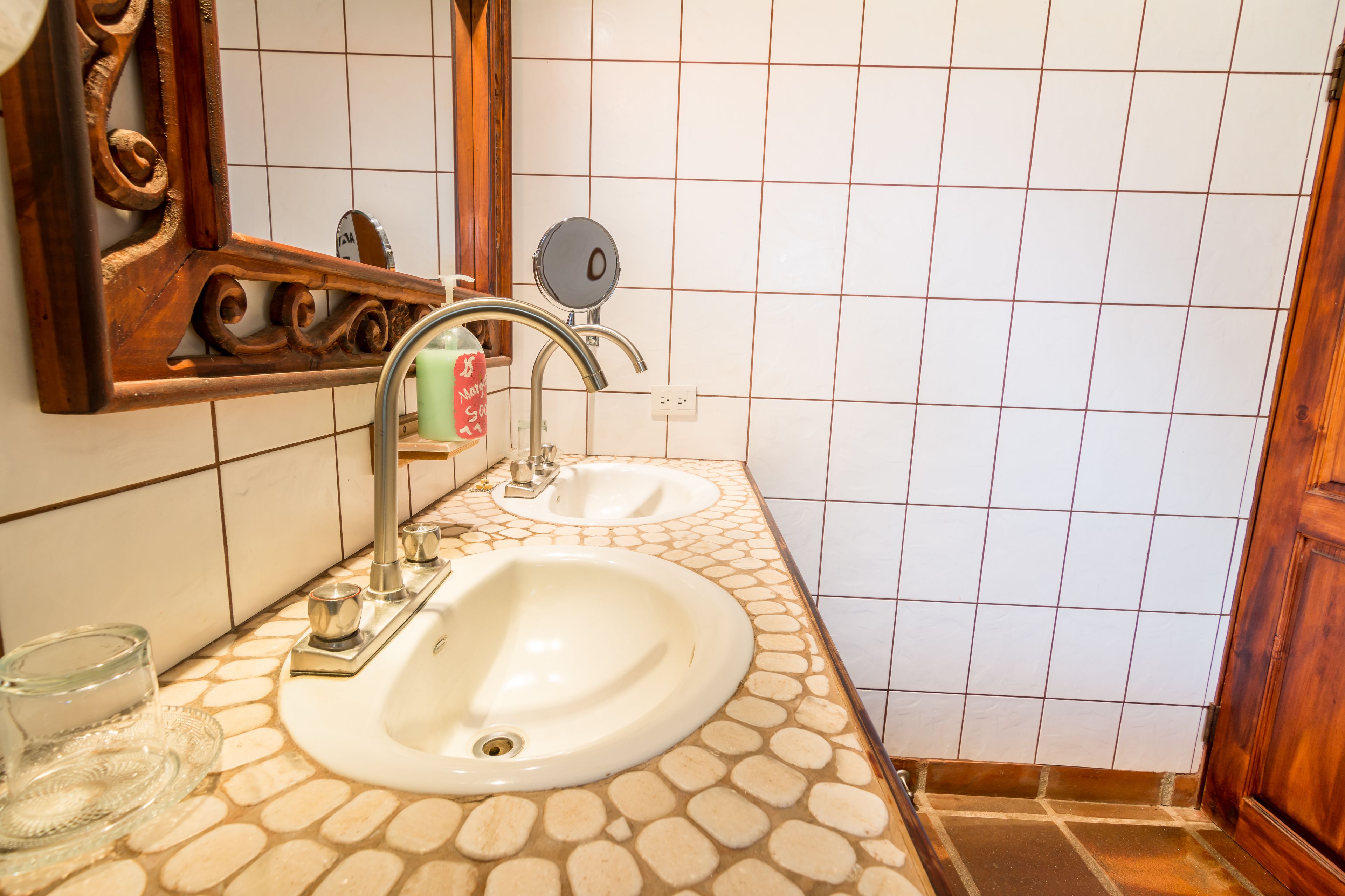 Un baño con dos lavamanos, un espejo y piso de baldosas.