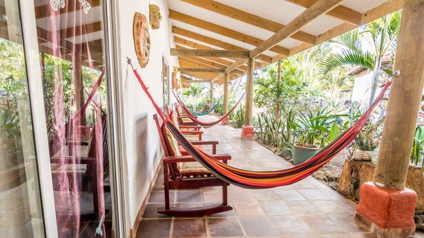 A covered outdoor area with wooden benches and a hammock, surrounded by potted plants and a tiled floor. - Villa Margarita (La Garita)