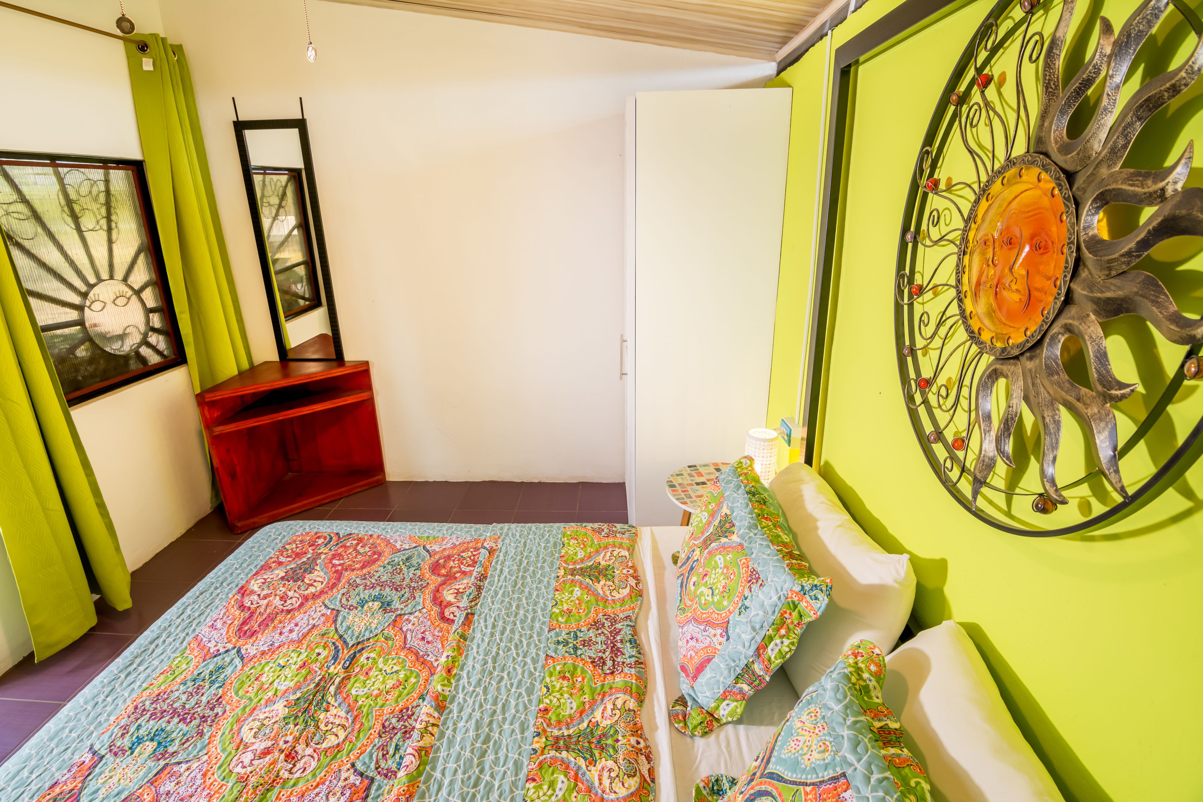Un dormitorio con una cama, un banco rojo, un espejo y un adorno en la pared.