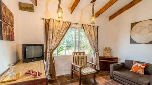 A cozy living room with a wooden TV stand, a cushioned chair, a sofa, and a dining table with a glassware set. - Villa Margarita (La Garita)