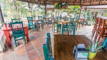 Een restaurant met houten tafels en stoelen, potplanten en een betegelde vloer.