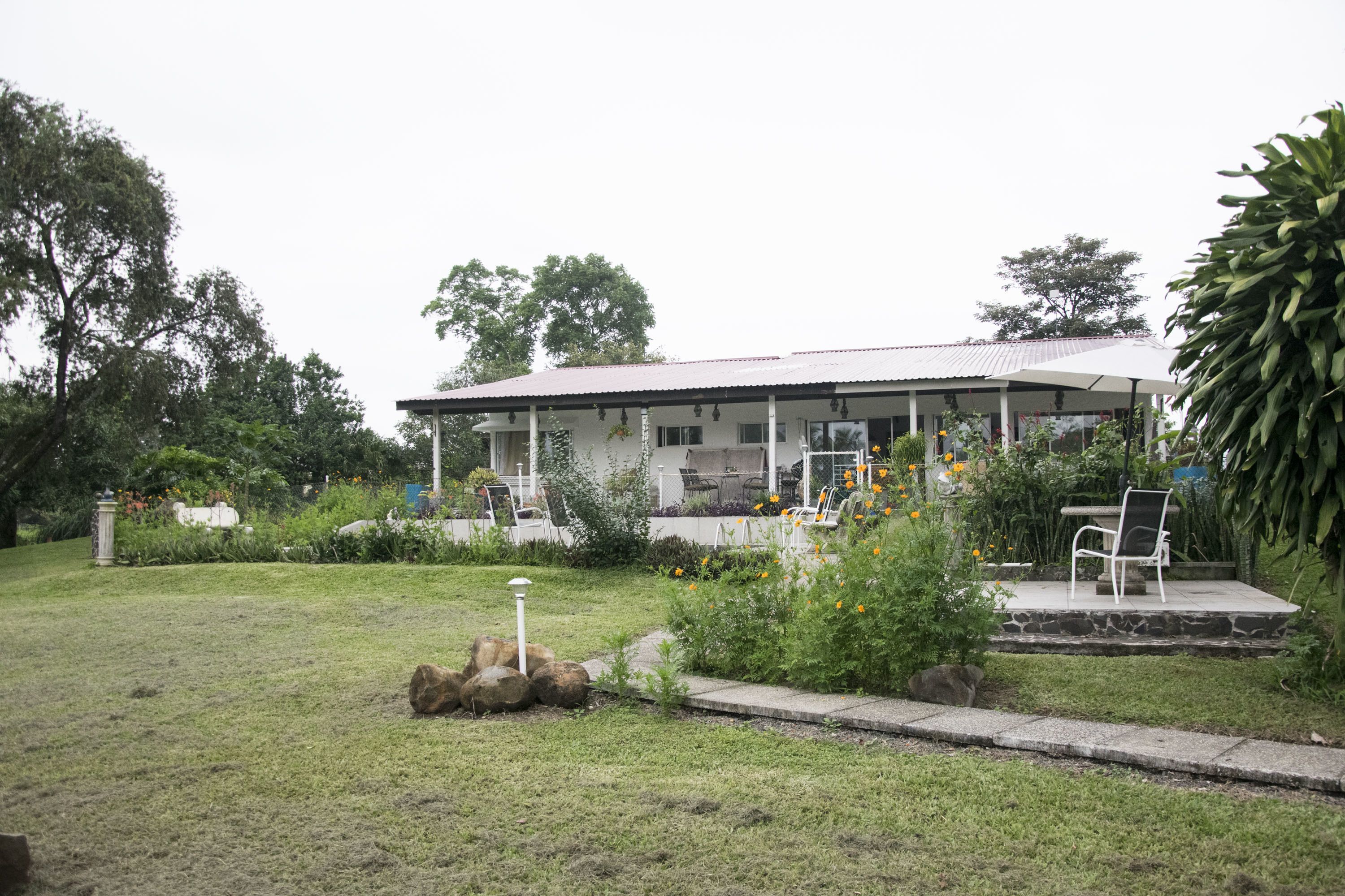 Una casa con porche cubierto, césped y un jardín con plantas y flores.