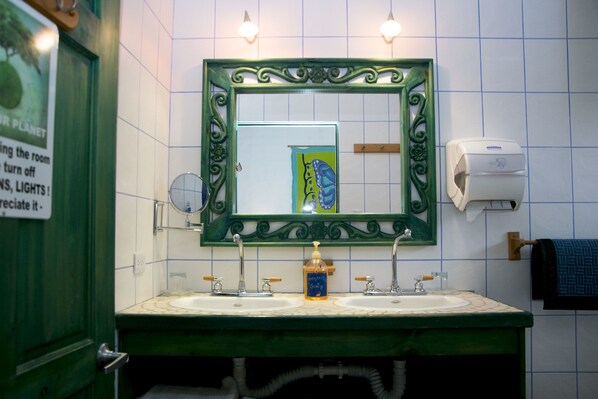 Un baño con dos lavamanos, un espejo con marco decorativo, un dispensador de jabón y un secamanos.