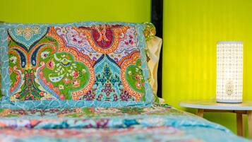 Una cama con una colcha estampada y colorida y una almohada decorativa frente a una pared amarillo brillante.