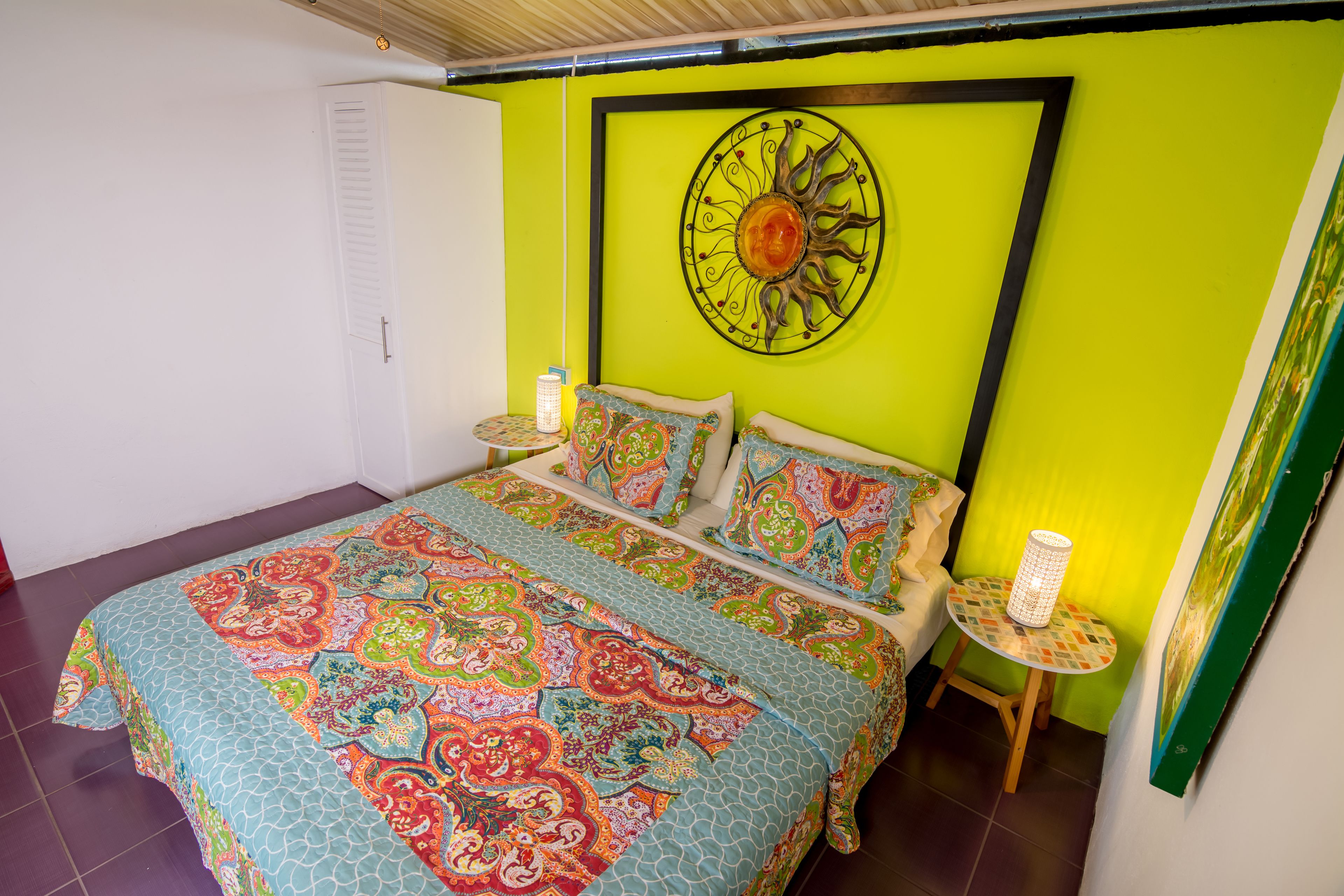 A bedroom with a bed, a wall clock, and a small table with a lamp.