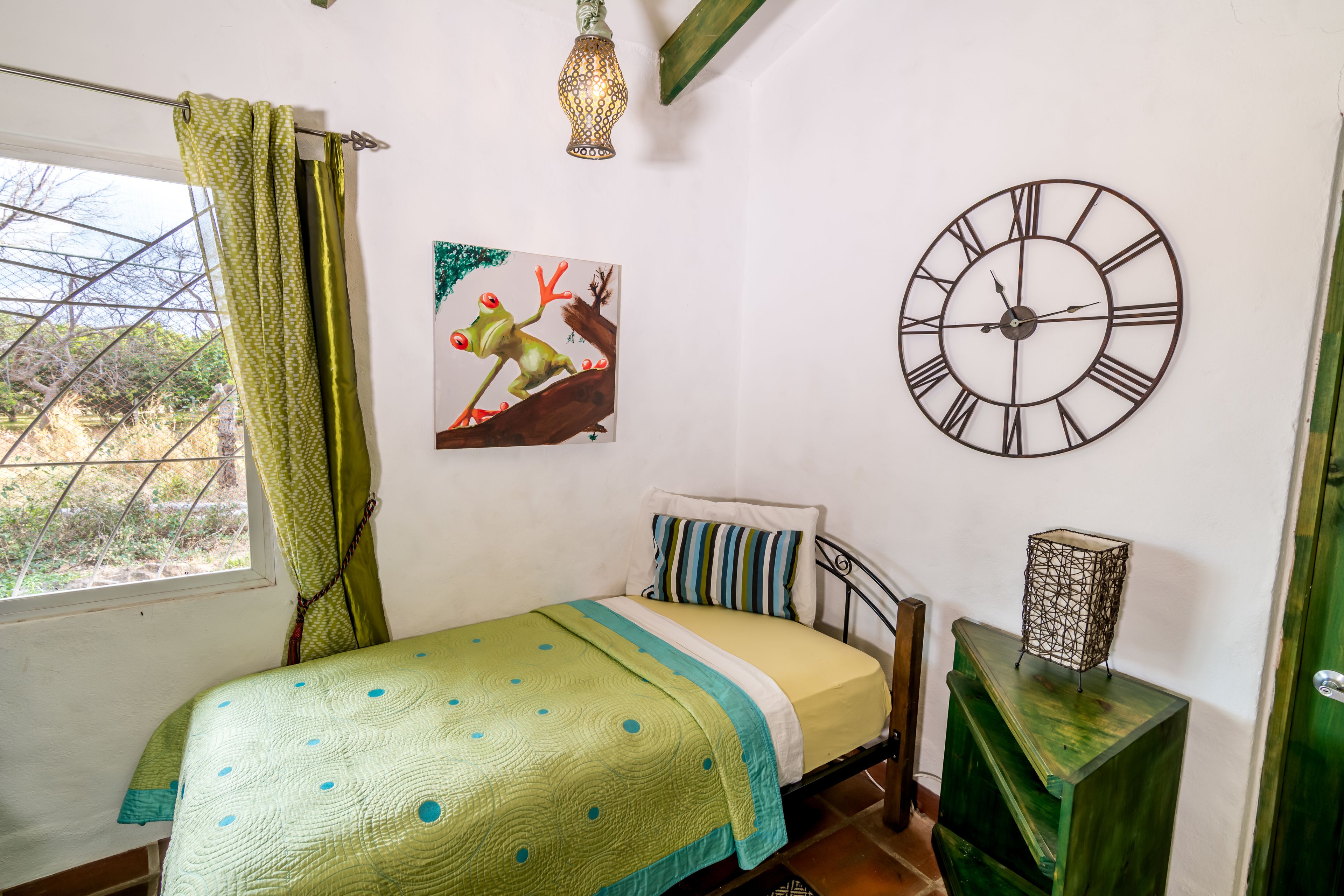 A bedroom with a bed, a wall clock, a painting, and a window with curtains.