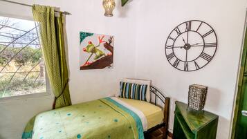 A bedroom with a bed, a wall clock, a painting, and a window with curtains.