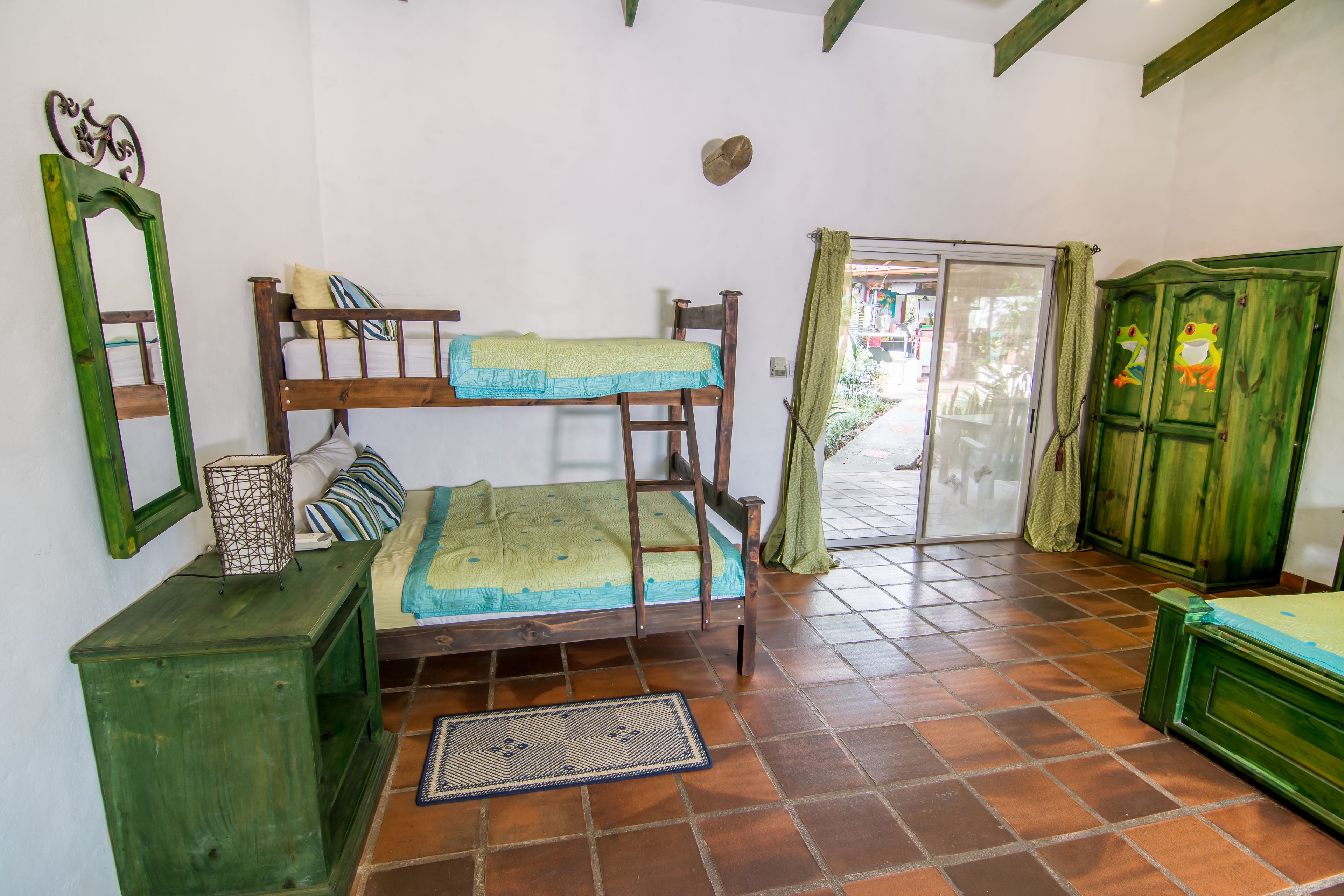 A room with a bunk bed, a wooden cabinet, a mirror, and a door leading outside.