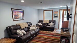A living room with a brown leather sofa, a wooden coffee table, a striped rug, and a TV stand with electronic devices. - Cozy and comfortable 3 bedroom.   (Alton)