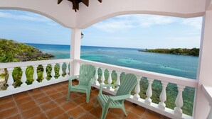 Un balcon abrité avec deux fauteuils Adirondack verts, une balustrade blanche et une vue sur l’océan.