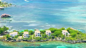 Vista aérea do Coral Vista Roatan, mostrando um conjunto de edifícios brancos com telhados vermelhos, rodeados por vegetação exuberante e águas turquesa cristalinas.