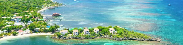 An aerial view of Coral Vista Roatan, featuring a cluster of white buildings with red roofs, surrounded by lush greenery and clear turquoise waters. - Experience An Oasis of Luxury in Roatan's Vibrant West End (Roatan)