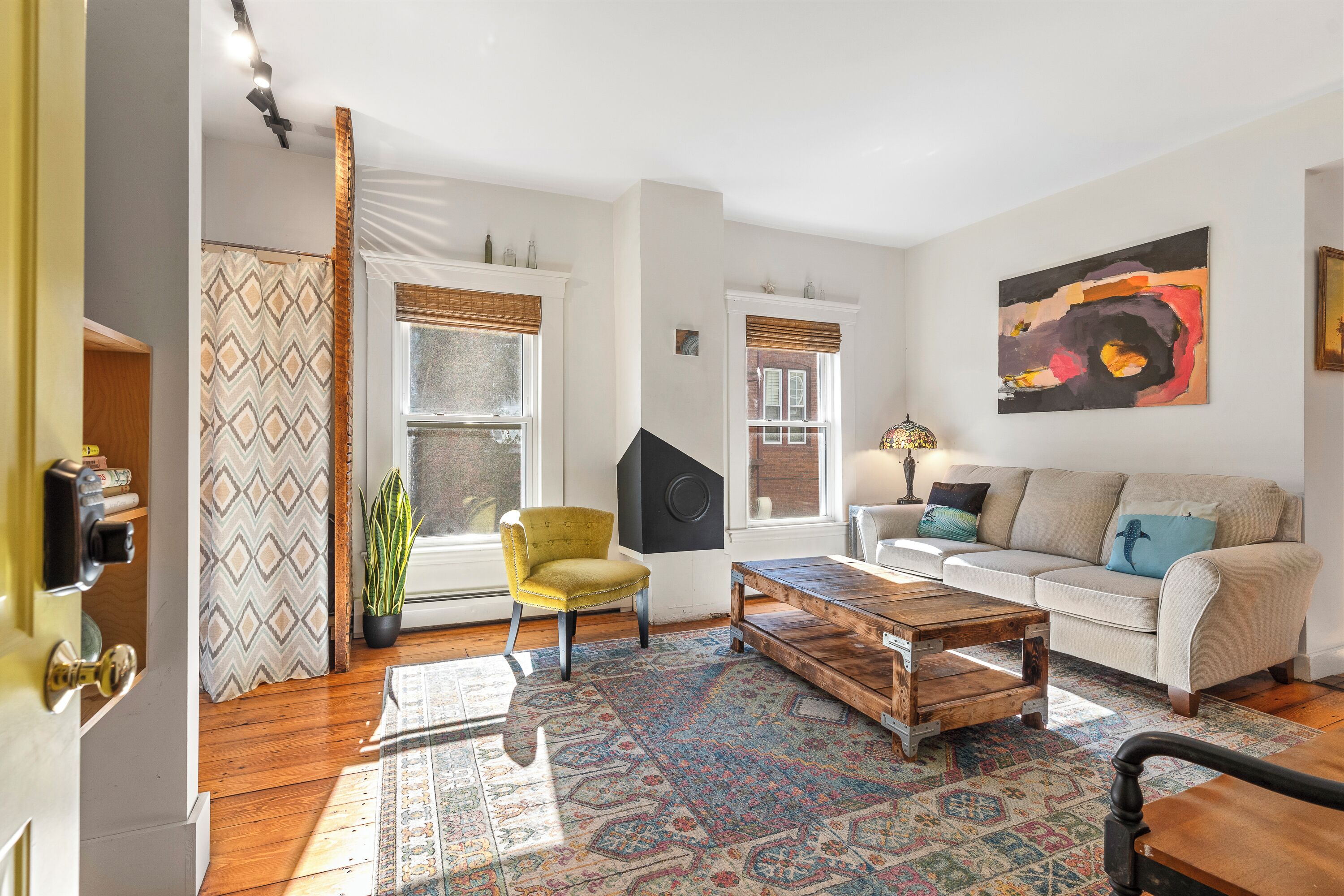 A living room with a sofa, armchair, coffee table, patterned rug, and a painting on the wall.
