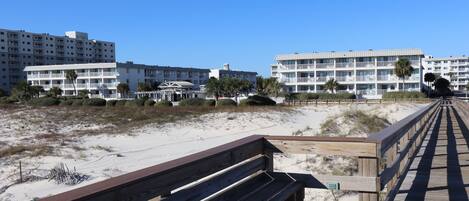 Una pasarela de madera que conduce a una zona de playa con edificios al fondo.