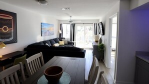 Una sala de estar moderna con un sofá negro, una mesa de comedor y una cocina visible a través de una puerta abierta.