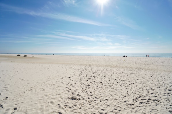 Une vaste plage de sable, parsemée d’empreintes, et un ciel dégagé.