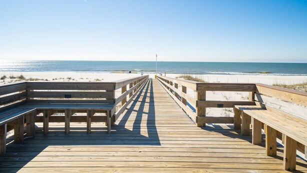 Un muelle de madera que conduce a la playa, con bancos y una bandera.