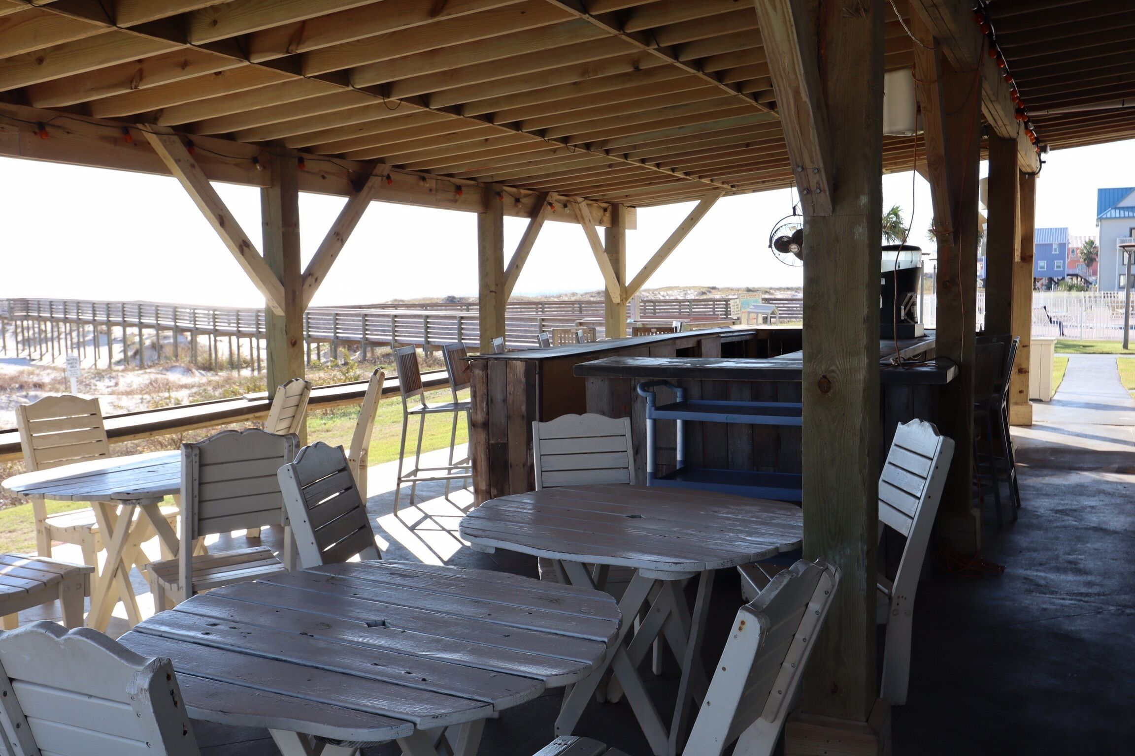 Eine überdachte Terrasse im Freien mit Holztischen und -stühlen, einer Bar und Blick auf eine Brücke und die Landschaft.