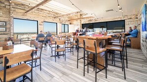 Un restaurante moderno con mesas y sillas de madera, ventanas amplias y un techo alto con vigas a la vista.