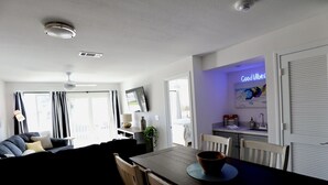 Una sala moderna con una mesa de comedor de madera oscura, un sofá y una cocina con un cartel que dice 'Good Vibes'.
